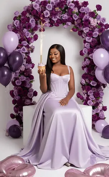 PROMPT : Transforme mon image en un portrait glamour d'une jeune femme (même visage et même teint)aux longs cheveux foncés et lisses, maquillage prononcé avec des lèvres brillantes, assise sur un cube blanc brillant. Elle tient un cupcake avec une fontaine lumineuse en train de s'allumer. Elle porte une robe de soirée bustier en satin lilas ou lavande clair, style corset, ajustée au niveau du buste et de la taille, avec une jupe longue et évasée. Ses jambes sont légèrement pliées. En arrière-plan, un arc dense de roses de couleur violet foncé à lilas est suspendu, créant un fond floral luxuriant. Des ballons de couleur violette, de différentes nuances, sont également dispersés à l'arrière-plan, notamment flottant sur les côtés. Au premier plan, de grands ballons en aluminium brillants  sont visibles. Le sol est blanc et le fond est un mur de studio blanc pur, avec un éclairage doux et flatteur qui crée des ombres minimales et un aspect propre et lumineux. La composition est centrée, le corps entier de la femme est visible. Le style de photographie est glamour et élégant, avec une esthétique de photographie de mode haut de gamme pour un anniversaire. #gemini #tiktok #texte